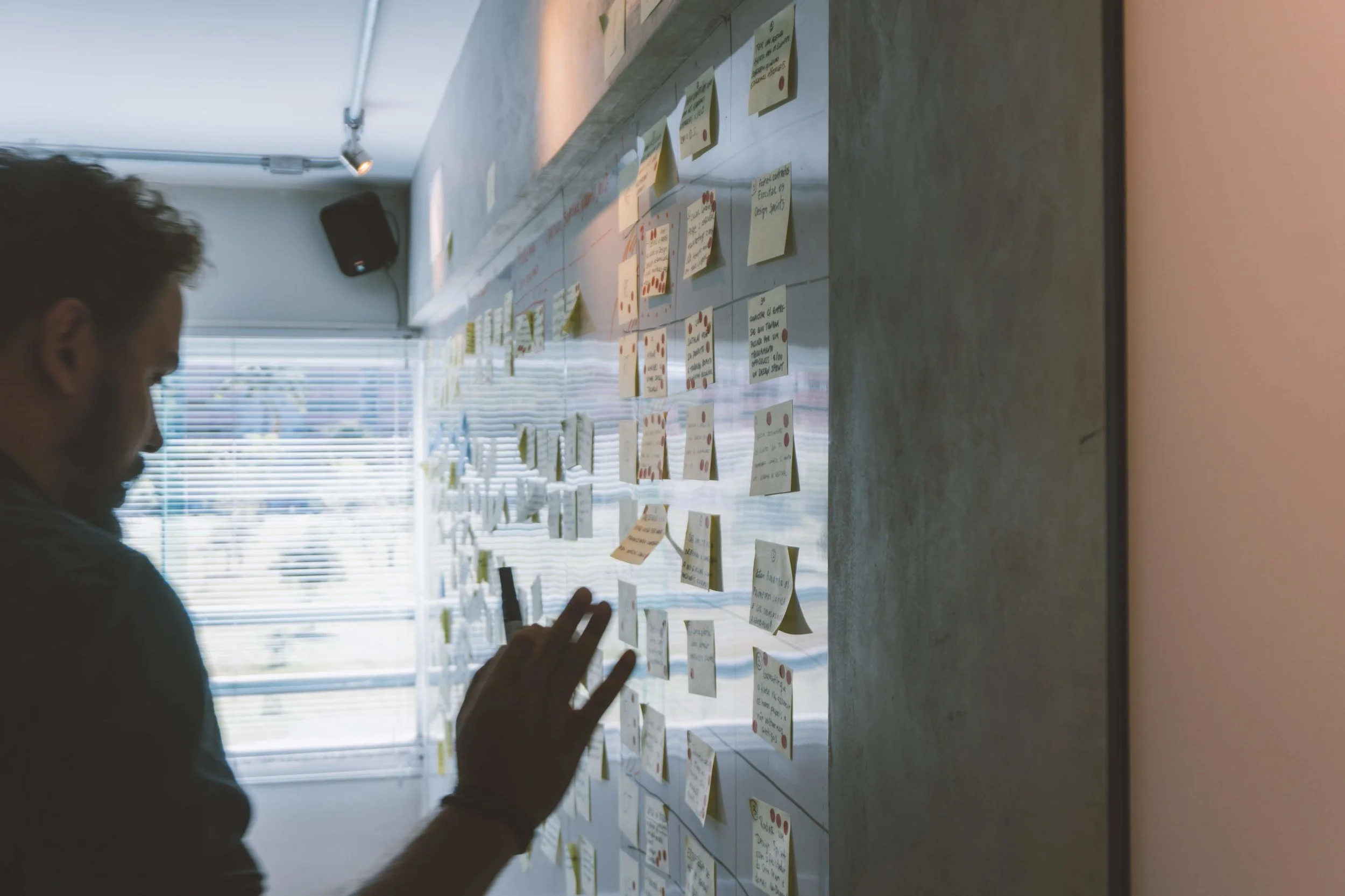 A person reviewing sticky notes on a glass wall during a design sprint session